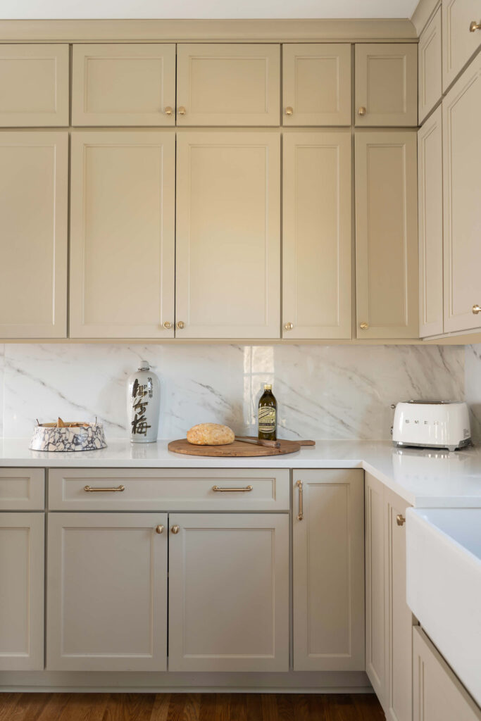 A kitchen corner with custom cabinetry by Holly Thompson Design, with cabinetry up to the ceiling and a marble slab backsplash.