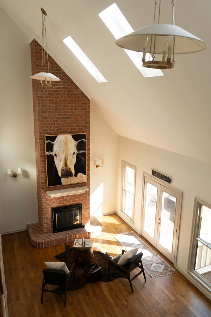 An open living room with skylights in the sloped ceilings, custom lighting and a large brick fireplace.