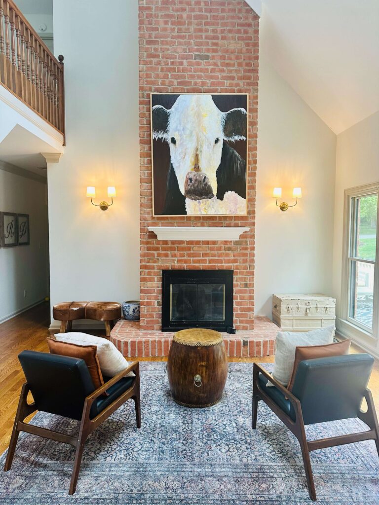 Custom living room with a large brick fireplace, lots of lighting and mid century arm chairs. The painting and stair railing are original to the homeowner.