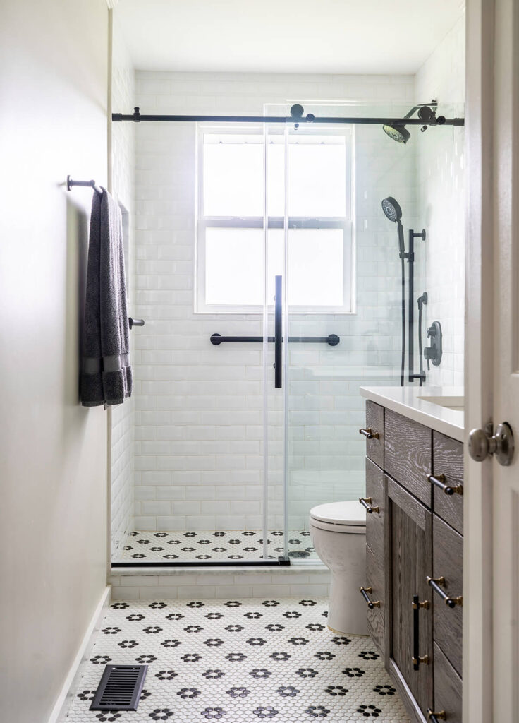 An overall picture of an updated bathroom with white walls, a dark wood vanity, and patterned black and white tile flooring.