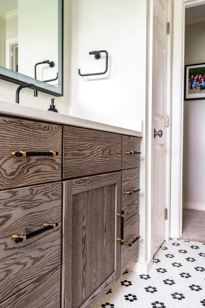 The vanity in a guest cottage bathroom, with a natural wood finish and black and gold hardware