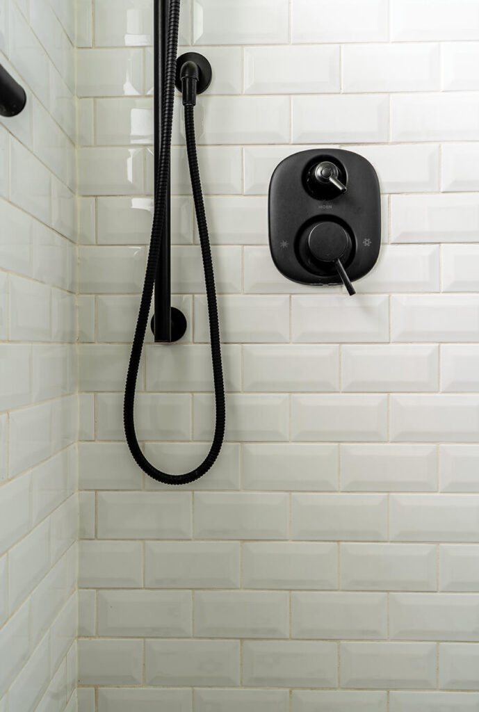 A close up of shower walls with white subway tile and black shower hardware