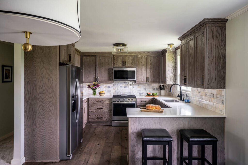 An overall view of the guest cottage kitchen, with bright features and masculine elements like black barstools and a natural wood finish on the cabinets.