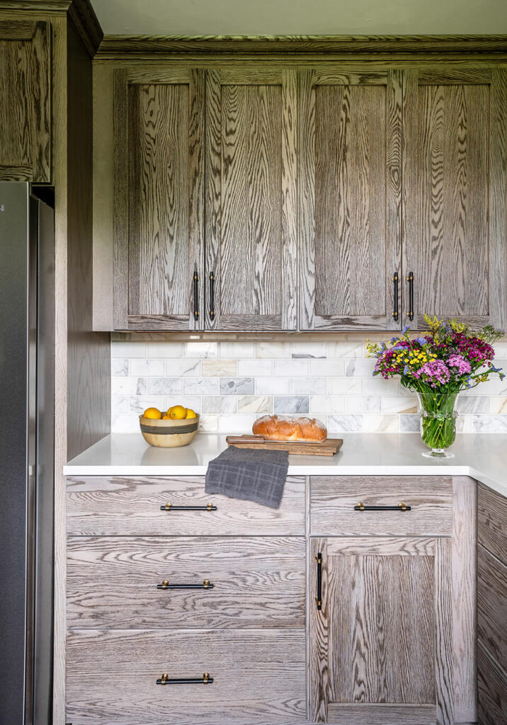 A section of the guest cottage kitchen with dark wood finish cabinets and a loaf of bread ready to cut on the countertop, and a vase of flowers.