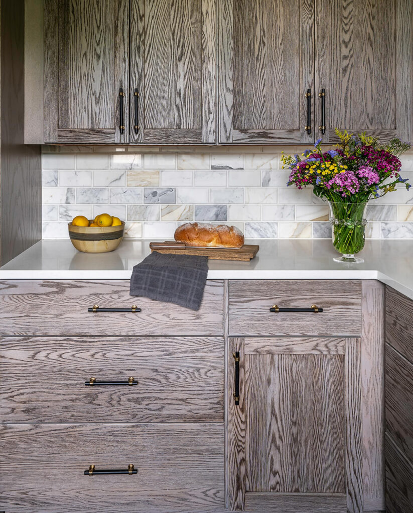 A section of the guest cottage kitchen with dark wood finish cabinets and a loaf of bread ready to cut on the countertop.