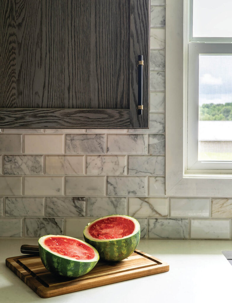 A window overlooking the countryside next to the kitchen sink, with a cutting board and watermelon.