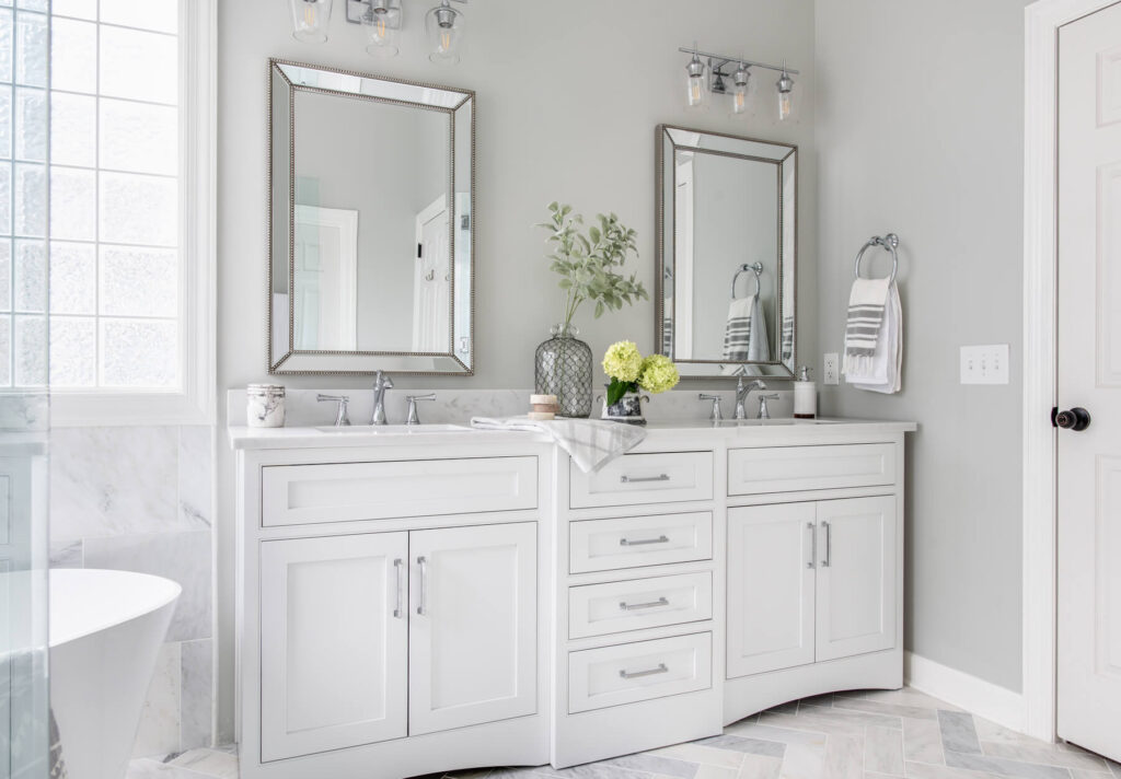 Two side-by-side white custom bathroom vanities with chrome faucets and vanity lighting.